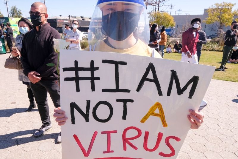 洛杉矶唐人街一名戴口罩和透明面罩的华裔女子，手持“我不是病毒”标语。（图：法新社）