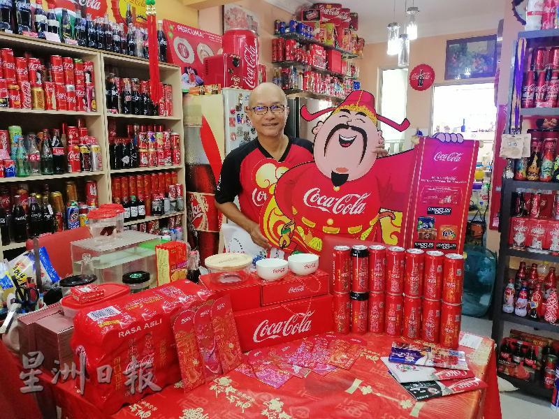 刘富威手持可乐财神造型广告牌，还有展示新年主题罐装可乐及红包封，向《星洲日报》读者拜早年！