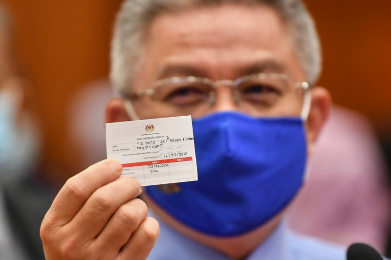 阿汉峇峇在完成模拟接种疫苗程序后展示疫苗卡。