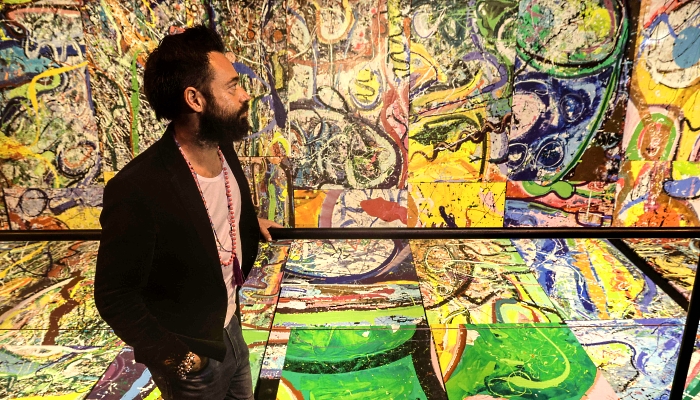 Dubai-based contemporary British artist Sacha Jafri walks in front of fragments of his painting entitled 