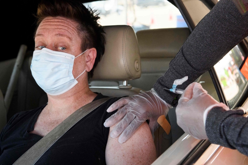 洛杉矶联合学区，一名教师在一处停车场设立的疫苖得来速接种点，让医护人员为她施打莫德纳冠病疫苖。（图：法新社）