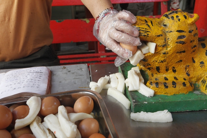 吉隆坡仙四师爷庙的助理协助善信将肉和蛋放入白虎的口中，寓意盼白虎吃饱后，不再伤人及说是非。