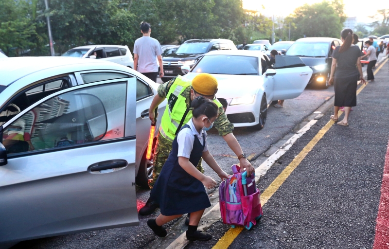 一名志愿警卫协助学生取书包下车。（图：星洲日报）