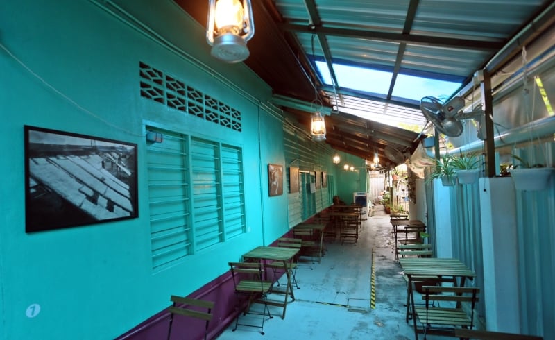 “安邦 Kopi 茶铺”（安邦总行）是罗国健婆婆的老家，70 年代时同为经营茶室，墙上吊挂的照片为安邦新村上个年代的点点滴滴。