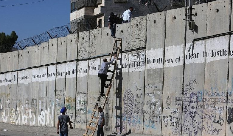 Palestinians climb over a section of Israel's separation wall near Qalandia checkpoint between Ramallah to enter Jerusalem. AFP