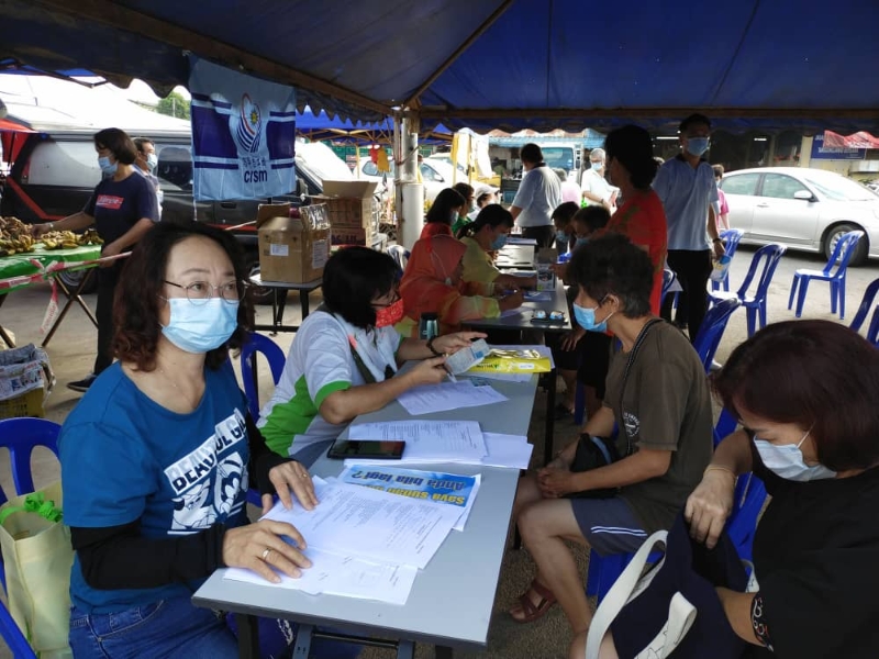马华志工团员协助民众填写登记接种疫苗表格。