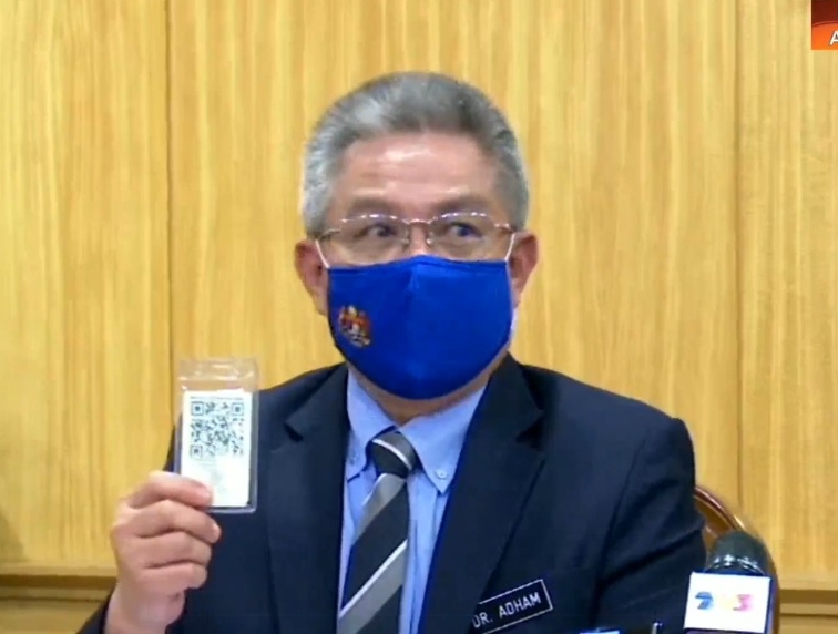 阿汉峇峇上展示“冠病疫苗卡”，并指每张卡都有安全码。