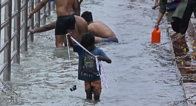 A boy carries a string with magnets to fish out coins thrown by devotees. AFP