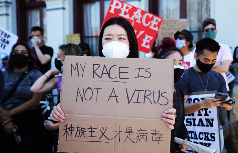 一名亚裔女子以中英文写道“我的种族不是病毒，种族主义才是病毒”。