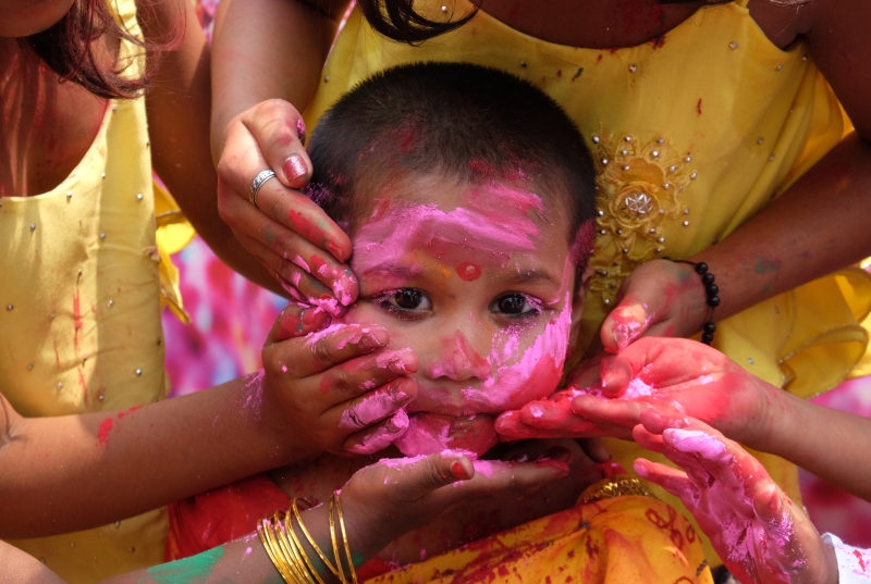 一名儿童被长辈们涂抹色彩, 传递满满的祝福.

