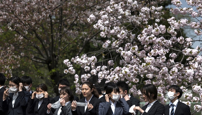 Company employees pose for photographs with cherry blossoms as a backdrop during the April 1 traditional first day of work for freshly-hired graduates, in Tokyo. AFP
