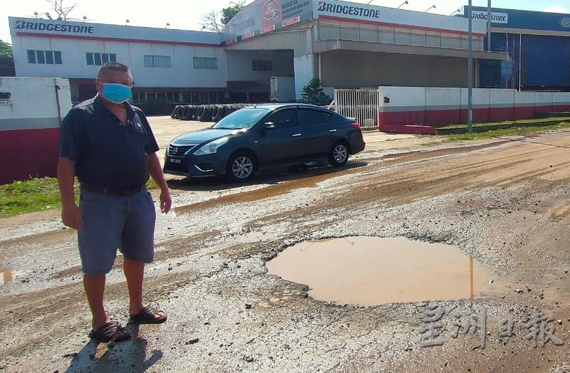 邱财汽向记者展示其轮胎厂前的路坑，因被废铁回收厂罗里碾坏积水。