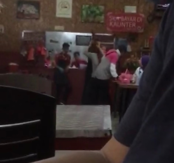 背对镜头的送餐员，在餐馆内遭掌掴颈部左侧。（脸书视频截图）