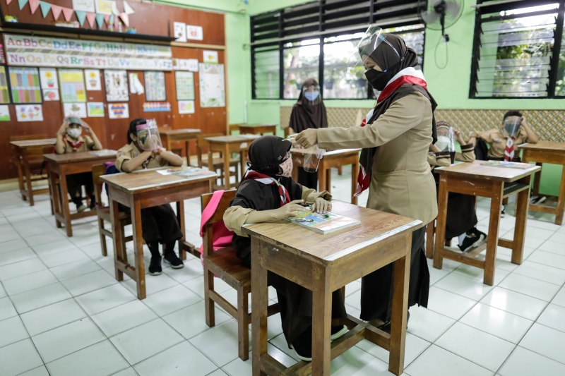 雅加达有学校测试校园重开时的上课情景，老师及学生都戴口罩及防护罩，桌位保持社交距离，上课前，老师为学生测量体温。（欧新社照片）

