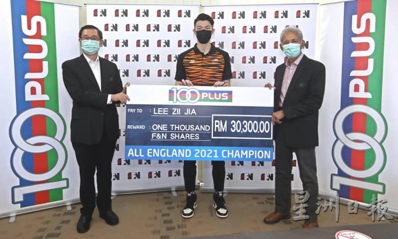 全英赛冠军李梓嘉（中）获得100 PLUS奖励价值3万零300令吉的股票。图为他从星狮控股的主席主席东姑赛巴达鲁丁（右）和首席执行员林友和（左）手中接领该奖励。