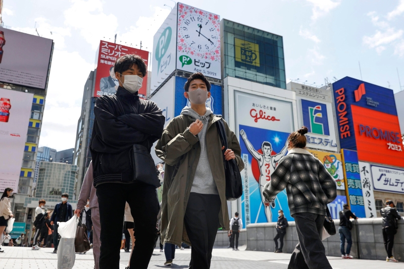 大阪地区最近成为日本疫情最严重的区域，6日的确诊病例更达到719例。图示戴着口罩的行人走在大阪道顿堀著名的Glico跑者大型广告牌前的画面。（美联社照片）