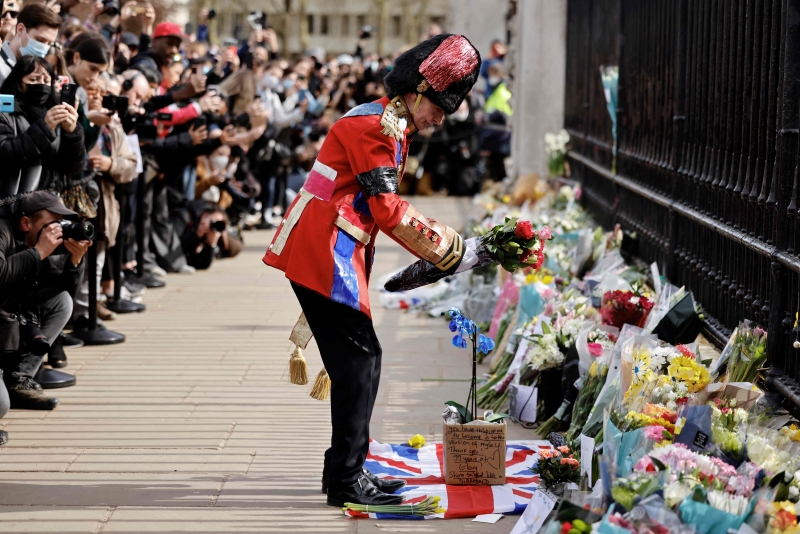 一名男子在白金汉宫门前摆放鲜花，寄托哀思。