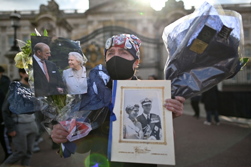 一名男子手持英女王及菲腊亲王照片和花束，在白金汉宫外追悼菲腊亲王。