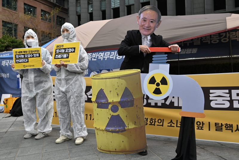 2名穿著保护服的韩国环保份子和一名穿著日本首相菅义伟面具的集会者，在抗议集会上“同台”。（法新社照片）