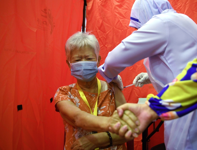 来自关丹的洪奶奶（80岁）在医护人员帮她注射疫苗时，抓紧在一旁陪伴的女儿的手。


