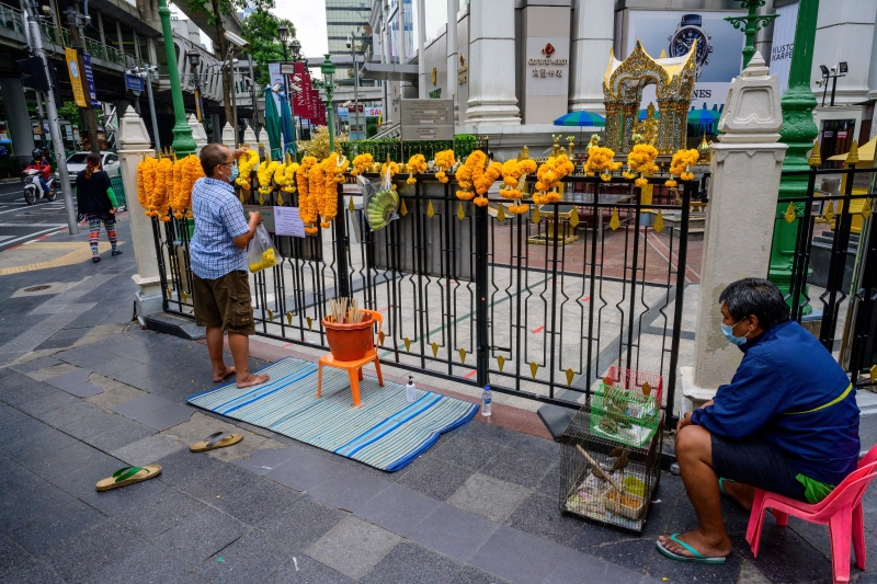 曼谷知名景区四面佛周一起被关闭，一名信徒只能在围篱外膜拜。（法新社照片）