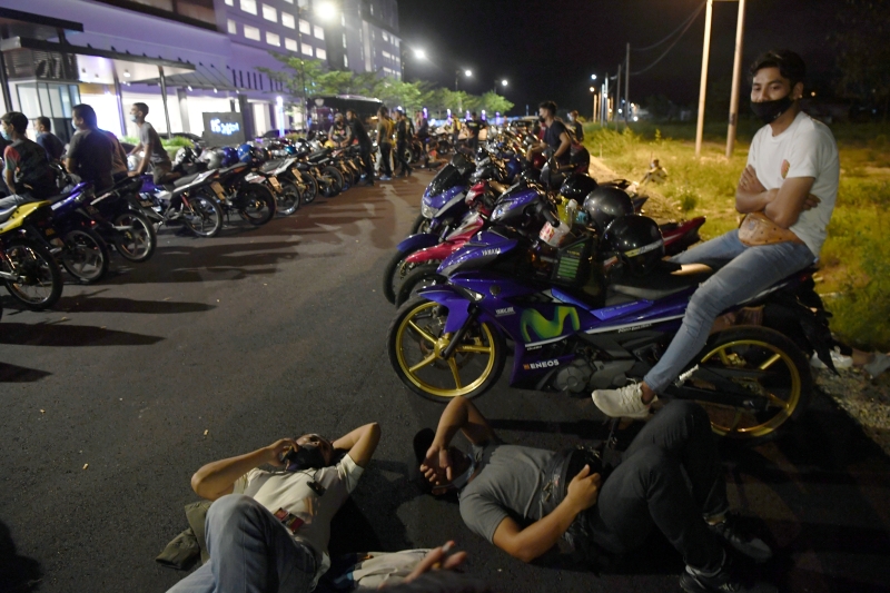 摩托车骑士或坐或躺在地上，等候警方开出罚单。（马新社照片）
