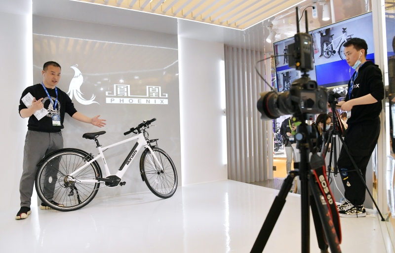 一家自行车品牌的工作人员在展位上以视频直播形式向不能前来展览的海外客户进行产品推介。（图：新华社）