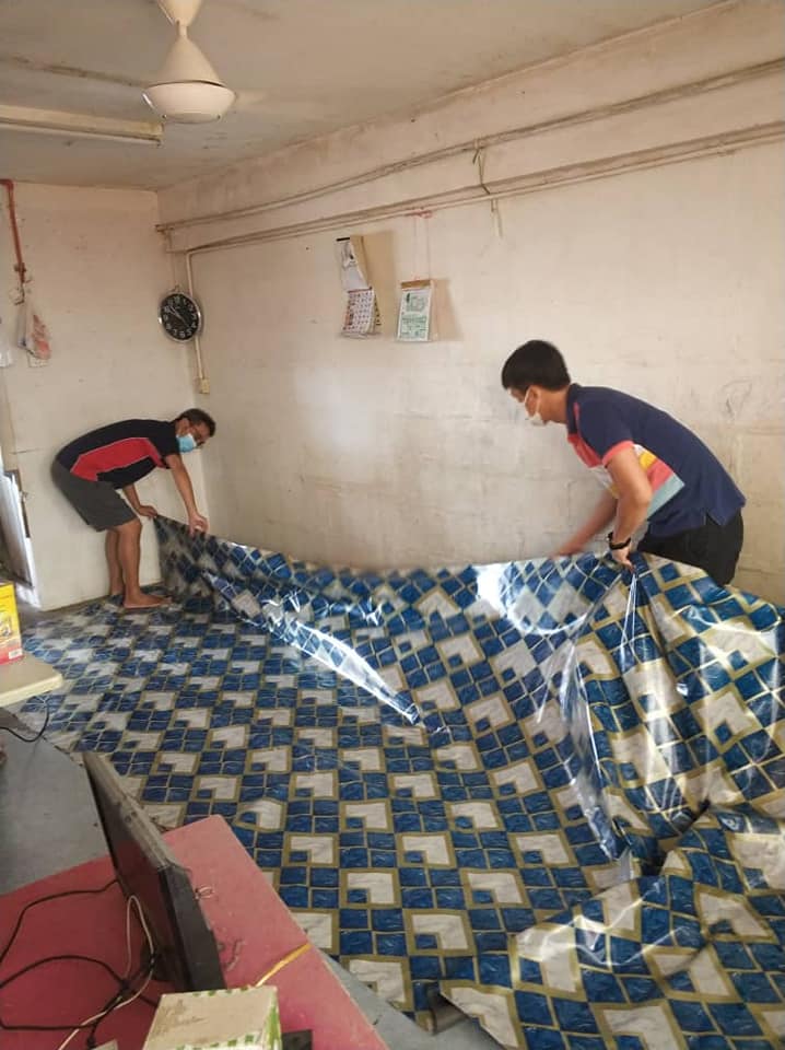 张晓峰（左）和副秘书骆行和把热心商家赞助的塑料地垫铺好，让学生家里更加整齐舒适。