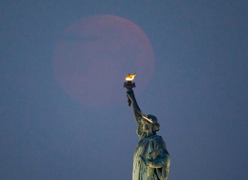 5月26日，在美国纽约，一轮圆月出现在自由女神像上方的天空。（图：新华社）