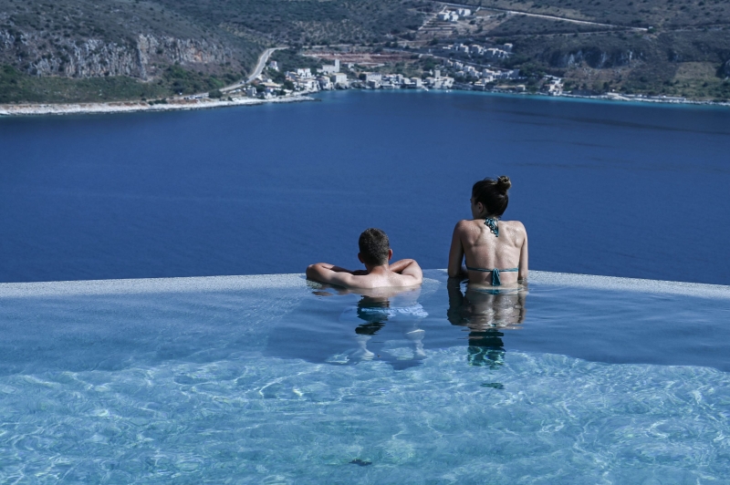 希腊开放旅游业后，一对情侣在南部伯罗奔尼撒半岛伊蒂洛一家酒店的泳池畅泳，期间凝视着眼前的蔚蓝大海。（图：法新社）
