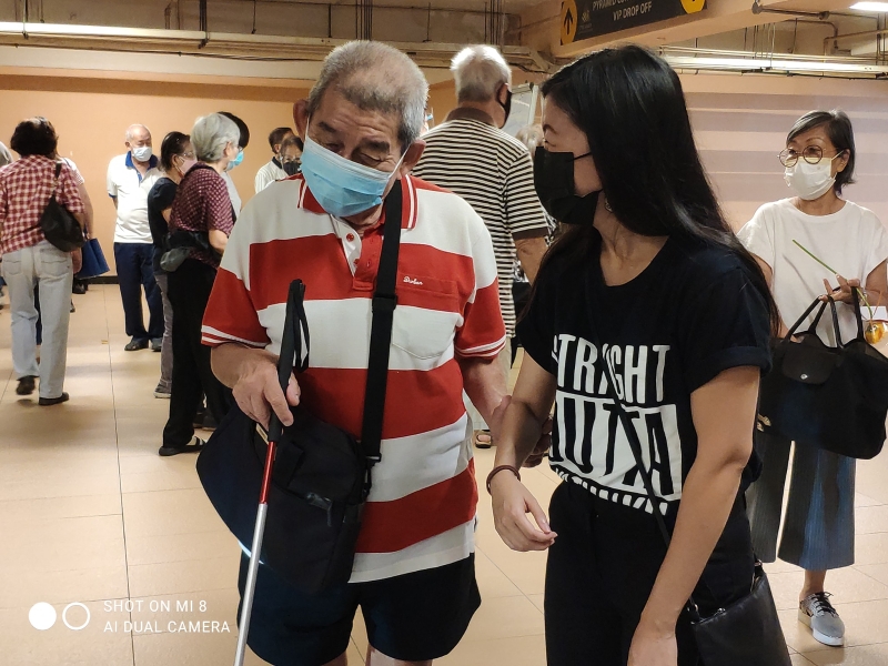 林怡威（右）协助一名半盲长者前往双威金字塔会展中心的疫苗接种中心。

