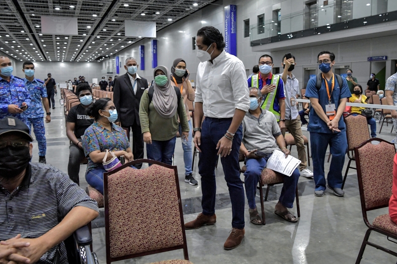 凯里（白衣者）巡视首日投入运作的吉隆坡城中城会展中心（KLCC）疫苗接种中心时，向接种者问好。