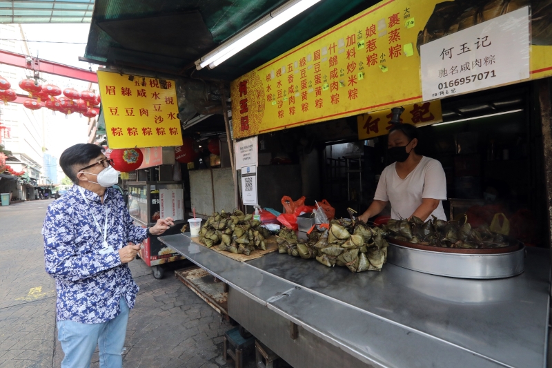 端午节即将来临之际，洪细弟（左）向售卖粽子的小贩了解今年的行情。

