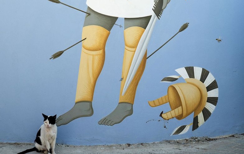 A cat sits next to a mural by Greek artist Fikos, who describes himself as a 