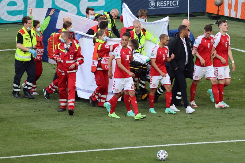 在埃里克森躺在担架被推出场外时，丹麦球员围着他缓缓前进，芬兰球迷也献上国旗让他遮挡。（法新社照片）