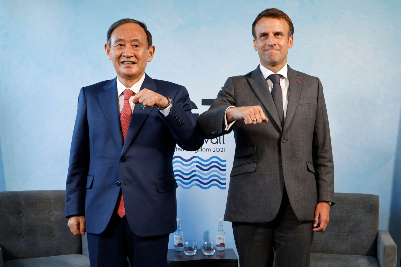正在出访的日本首相菅义伟（左）在G7峰会期间与法国总统马克龙（右）举行场边会议前行“碰肘礼”合照。（图：法新社）