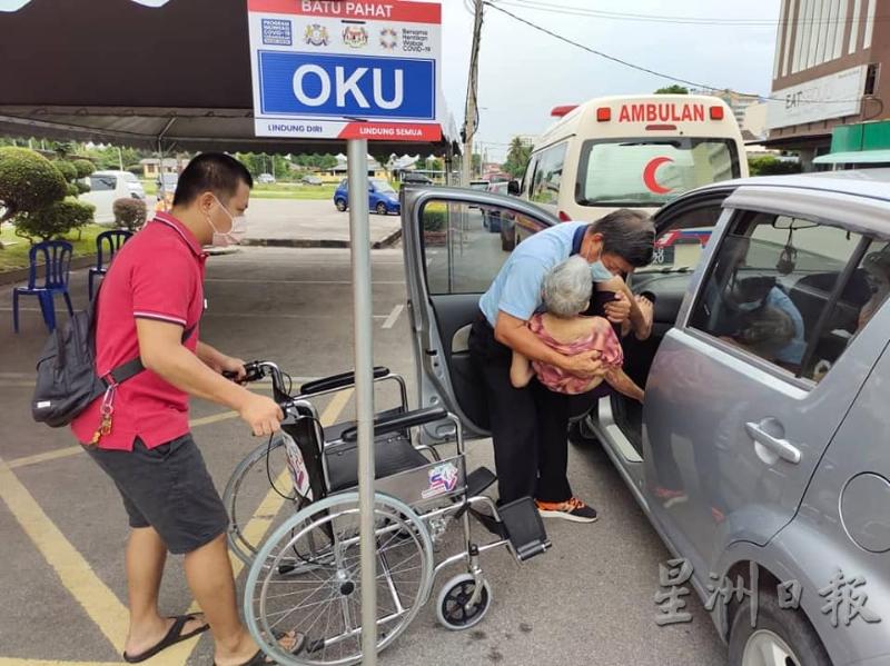 志工将行动不便的老人家抬抱下车，再使用轮椅将她送入场内接种疫苗。