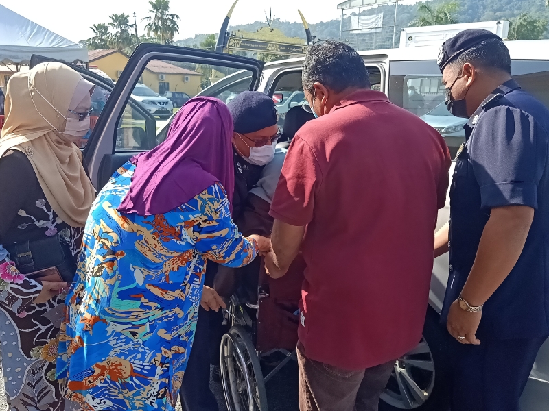  庇朥警区主任安然莫哈末甘尼（中）协助将一名行动不便的老人从车子内抬出到轮椅上。