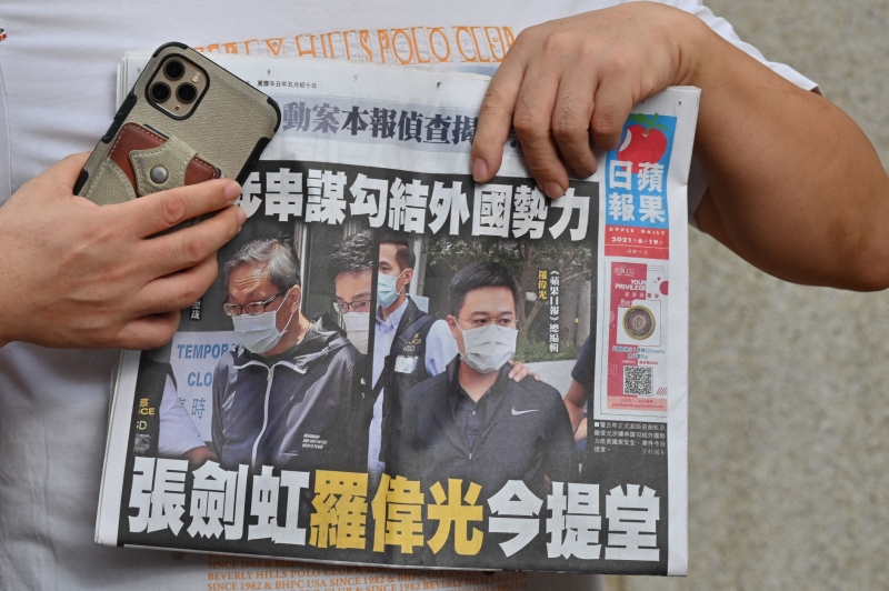 壹传媒行政总裁张剑虹、《苹果日报》总编辑罗伟光上周六提堂，一名民主活动人士手持《苹果日报》在法院外抗议。（法新社照片）
