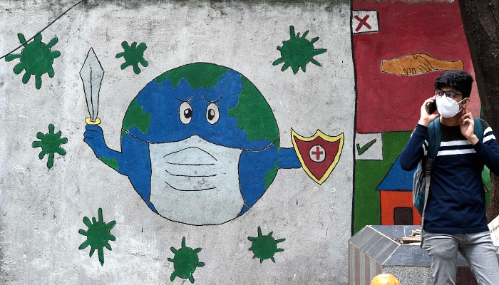 A college student speaks on his mobile phone near a wall mural depicting a planet earth with a face mask holding a sword and a shield to spread awareness about the coronavirus in Mumbai, India. AFP
