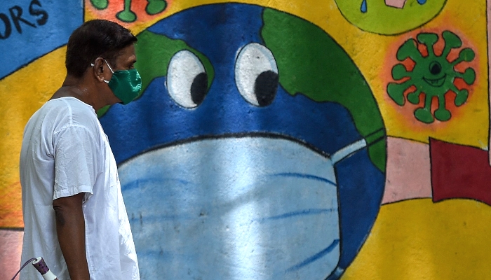 A man walks past a wall mural depicting a planet earth with a face mask to spread awareness about the coronavirus in Mumbai, India. AFP
