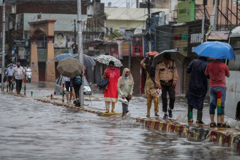 周一，印度季候风季节的暴雨在查谟地区造成水灾，街道被洪水淹没，路人只得在分界堤上行走。（美联社照片）