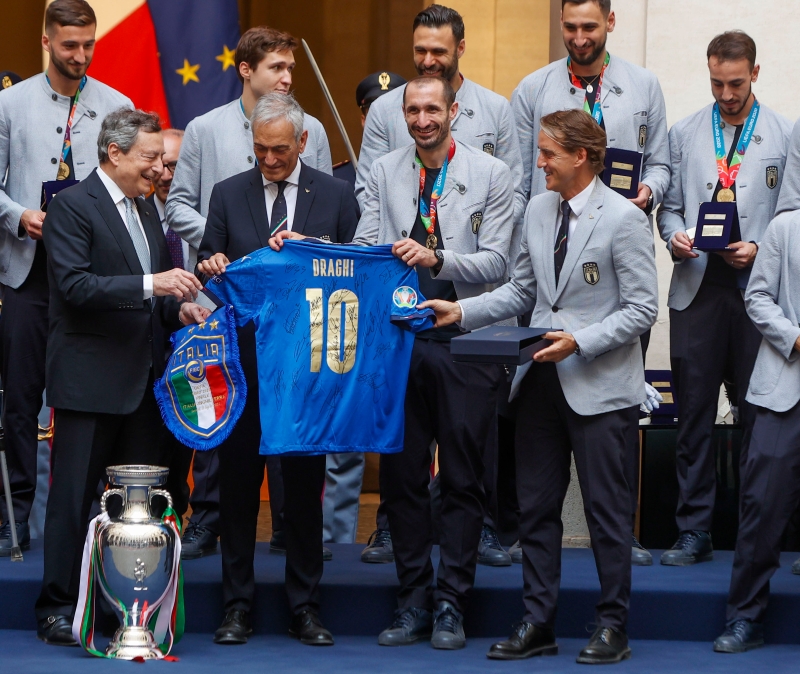 意大利足球队与意大利总理德拉吉会面，图为德拉吉（前排左1起）从意大利足总主席格拉维纳、队长基耶利尼和主帅曼奇尼手中接过纪念球衣。（美联社照片）