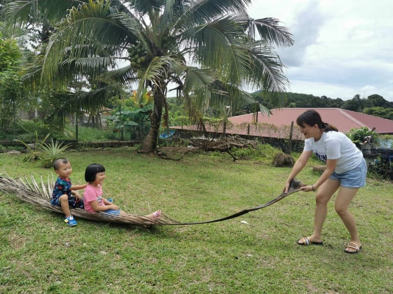 林晓仪用椰树的叶子，让孩子坐在上面拖拉着，开心的与孩子玩乐。