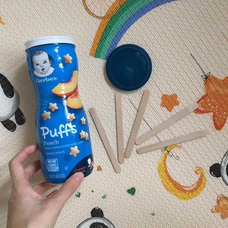 苏丽凤使用零食罐和冰淇淋木支制作玩具，让孩子学习将木支装入瓶内。
