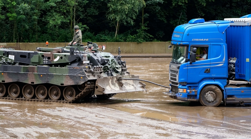 德国军队出动坦克赈灾，坦克车把卡车从泥潭拖走。