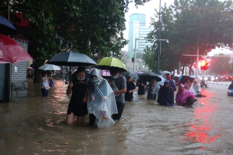 在强降雨后，郑州路面积水严重，许多民众被迫撑伞涉水而行。（图：美联社）