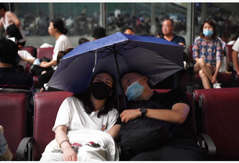 旅客滞留在郑州东站。候车厅出现漏雨情况，旅客撑伞挡雨。