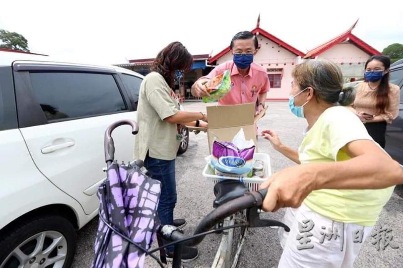 郑修强（左二）协助民众把所领取的物资放进脚车篮子。