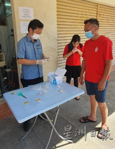 谢琪清（左）仿佛成了‘医护人员’，在做好防范措施下，协助服务中心内的工作人员进行冠病检测，右为拉杭新村村长刘秋兴。
